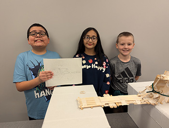 Three smiling students behind the bridge they built