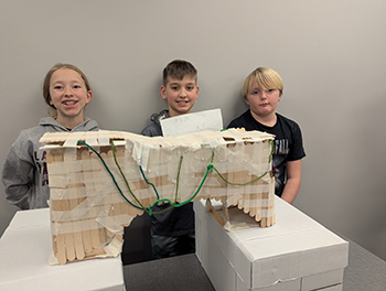 Three students standing by the craft stick bridge they built