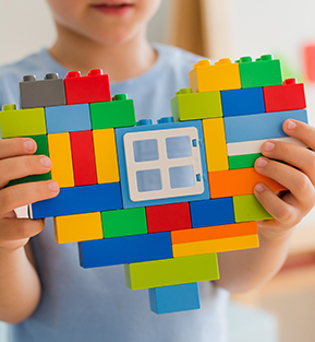 Child playing with plastic toy blocks and making a heart