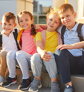 Group of four happy elementary students sitting outside