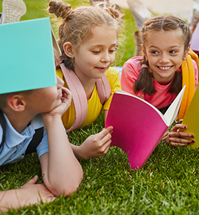 Group of happy elementary students on the grass with books