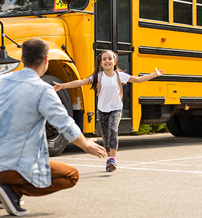 Happy school girl running to her parent from the school bus